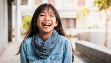 一位在戶外面帶燦爛笑容，穿著藍色衣服并圍著圍巾的少女