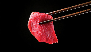 新鲜的牛肉片，色泽鲜红，纹理清晰，被一双筷子轻轻夹起