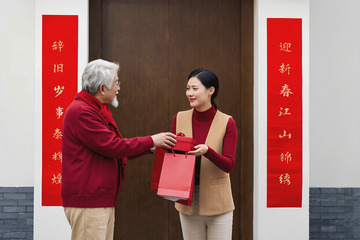 正将一个红色礼盒递给一位穿着红色上衣和米色背心的年轻女子