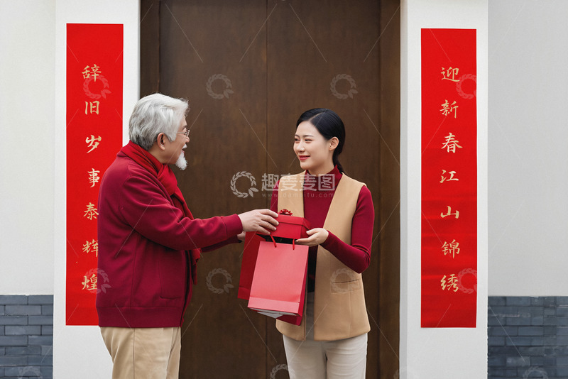 正将一个红色礼盒递给一位穿着红色上衣和米色背心的年轻女子