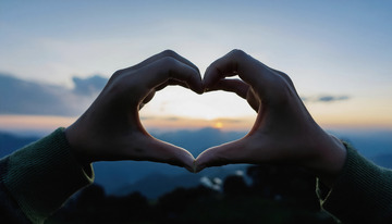 一双手在夕阳美景下比心的温馨画面
