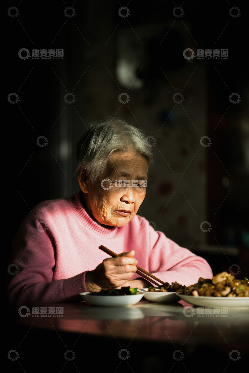 高清大图下载【趣麦麦图】-一位头发花白的老奶奶她穿着粉红色的衣服独自坐在桌前用餐桌上摆放着食物老奶奶神情专注画面光线集中在她身上周围环境略显昏暗营造出一种孤独的氛围仿佛在诉说着老年人独自生活的日常1
