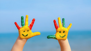 绿色等鲜艳色彩。小手高高举起，背景是蓝天和模糊的绿地或水面，充满童趣与活力。