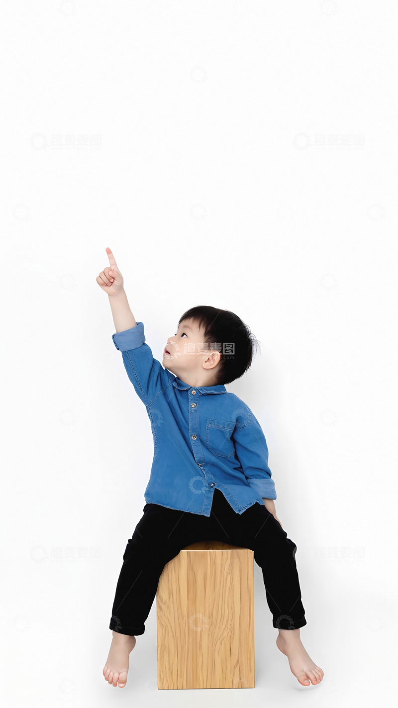高清大图下载【趣麦麦图】一个小男孩穿着蓝色牛仔衬衫和黑色裤子，光着脚坐在一个木质的立方体上。他的右手高高举起，食指指向上方，头部微微仰起，眼神看向手指的方向，似乎在好奇地指着什么