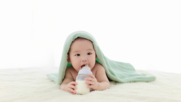 一个裹着浅绿色毯子的婴儿双手捧着奶瓶