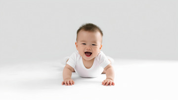 一个穿着白色衣服的婴儿，双手和双膝撑在白色的平面上，咧着嘴开心地笑着，展现出活泼可爱的模样