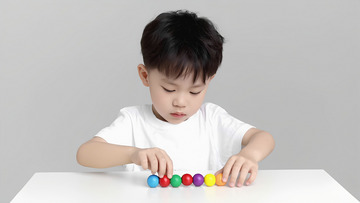 一个小男孩穿着白色上衣，正专注地坐在桌前玩彩色积木，他的双手在摆弄积木，神情认真投入