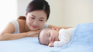 一位女士面带温柔的微笑，趴在一旁，目光柔和地看着正在蓝色毯子下熟睡的婴儿。整个场景温馨，充满母爱。