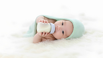 一个裹着浅绿色毯子的婴儿双手捧着奶瓶1