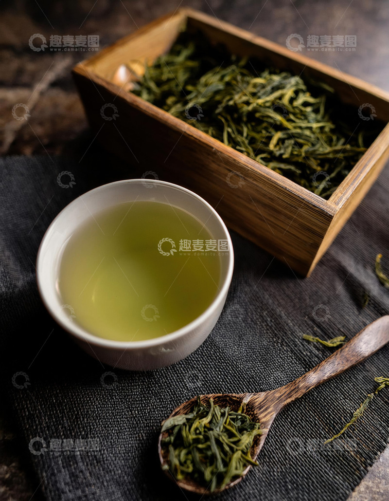 高清大图下载【趣麦麦图】茶勺，茶勺上和盒子里放着干绿茶，茶杯中盛有泡好的绿茶，茶汤呈现出淡绿色，背景是深色的布料，营造出一种古朴，雅致的氛围1