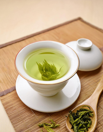 白色的茶壶，茶杯和茶托，杯中盛有泡开的绿茶，茶叶在茶汤中舒展开来，色泽嫩绿