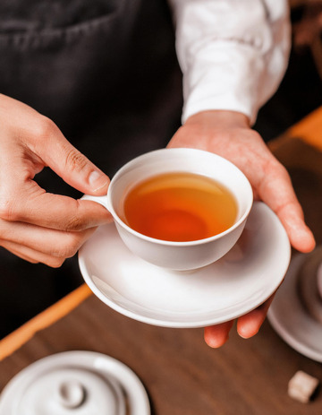 双手端起装有红茶的白色茶杯及茶托的场景3