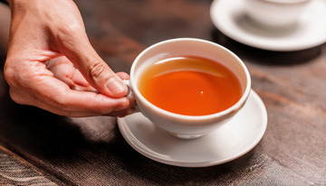 一只手端起装有红茶的白色茶杯及茶托的场景