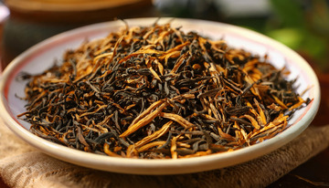 盘子里面装满了色泽乌润且带有金色芽毫的红茶茶叶，背景简单，突出了红茶茶叶的细节和质感