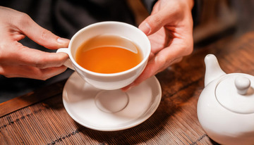 双手端起装有红茶的白色茶杯及茶托的场景