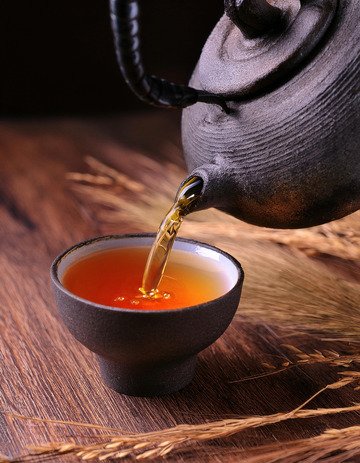 茶壶正往黑色的茶杯中倾倒橙红色的红茶茶汤，背景中有一些干草，营造出一种古朴