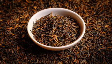 白色的碗，碗中装满了色泽乌润且带有金色芽毫的红茶茶叶，背景是大量散落的同款红茶茶叶，整体突出了红茶茶叶的质感与形态1