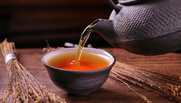 茶壶正往黑色的茶杯中倾倒橙红色的红茶茶汤，背景中有一些干草，营造出一种古朴3