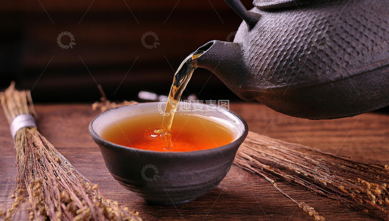 高清大图下载【趣麦麦图】茶壶正往黑色的茶杯中倾倒橙红色的红茶茶汤，背景中有一些干草，营造出一种古朴3