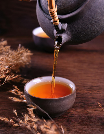 茶壶正往黑色的茶杯中倾倒橙红色的红茶茶汤，背景中有一些干草，营造出一种古朴1