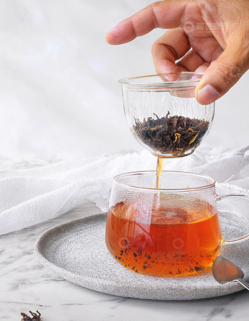 高清大图下载【趣麦麦图】一只手正拿着一个透明小茶杯，将其中的红茶茶叶倒入下方装有茶汤的透明大玻璃杯中