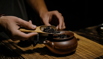 一双手正用木制茶勺将茶叶从容器舀入古朴的陶制茶罐中，背景是木质桌面和竹制茶席2