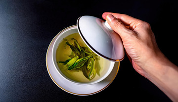 手揭开盖碗的画面,盖碗中装着泡开的嫩绿茶叶和淡黄色茶汤1
