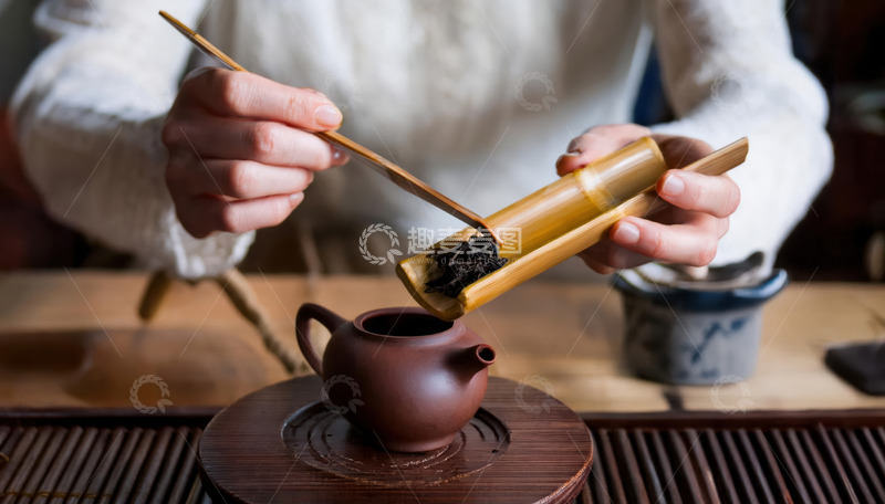 高清大图下载【趣麦麦图】-一双手正拿着竹制茶则，将茶叶倒入古朴的紫砂壶中，背景简单，展现传统的泡茶准备过程