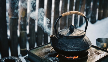 冰天雪地中，一个古朴的铁壶置于户外，壶口正冒着热气，背景是木栅栏1