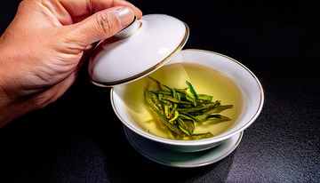 手揭开盖碗的画面,盖碗中装着泡开的嫩绿茶叶和淡黄色茶汤