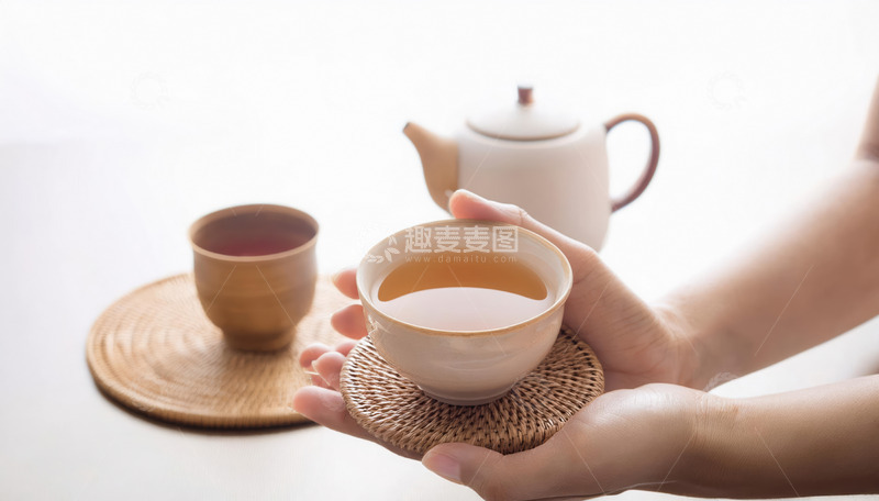 高清大图下载【趣麦麦图】一双手捧着置于编织杯垫上的茶杯，杯中盛有橙黄色茶汤，背景有古朴的茶壶和茶具2