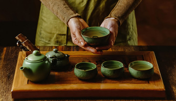 有双手正在操作茶具，包括拿起茶杯等动作，背景为深色，突出了绿色茶具的质感
