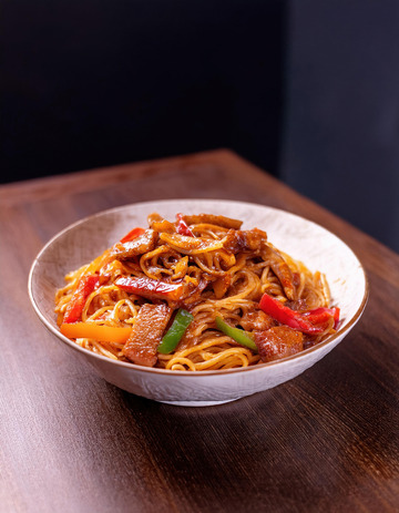 碗装在白色碗里的红烧肉盖面上面有青椒红椒和肉块摆在深色桌面上