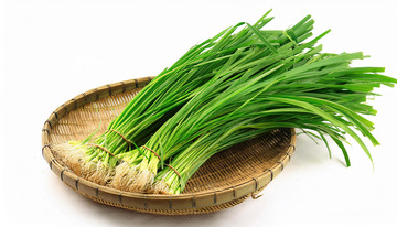 一把放在竹制托盘里的新鲜嫩绿韭菜
