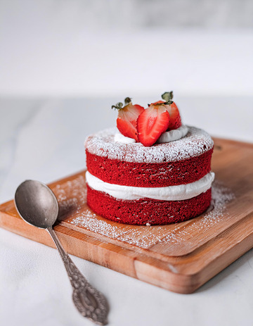 一块放在木制砧板上夹着白色奶油顶部有草莓装饰撒着糖粉的红色蛋糕旁边有银勺4