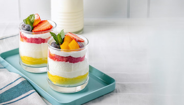 装在透明杯子里的水果奶油杯放在浅蓝色托盘上旁边有一瓶牛奶