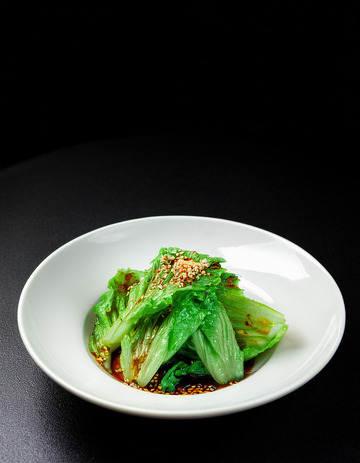 一盘装在白色圆盘中淋有酱汁撒着芝麻的生菜