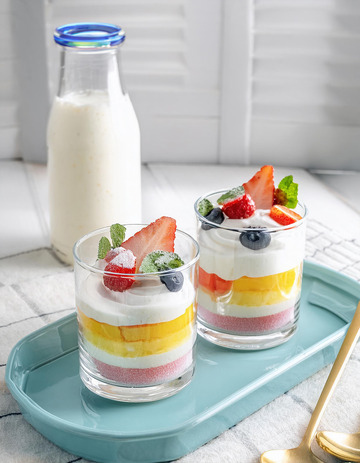 装在透明杯子里的水果奶油杯放在浅蓝色托盘上旁边有一瓶牛奶1