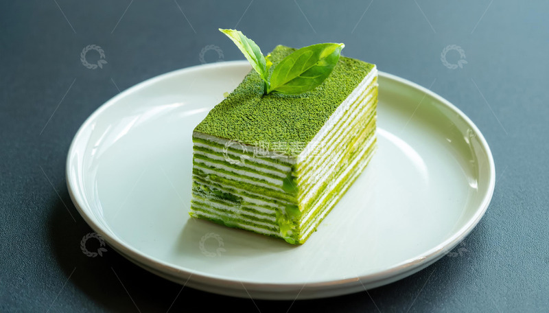 高清大图下载【趣麦麦图】-一块放在白色盘子上夹着白色奶油顶部有绿叶装饰的抹茶千层蛋糕1