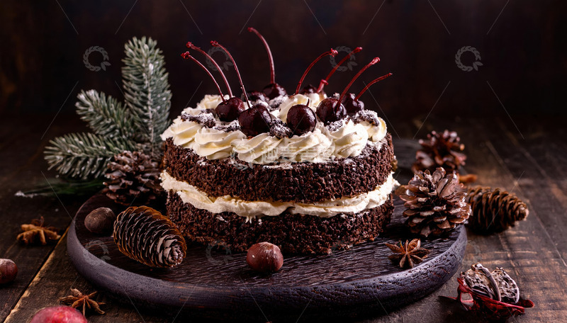 放在深色盘子上装饰有樱桃奶油和巧克力屑周围有松枝松果的巧克力蛋糕2