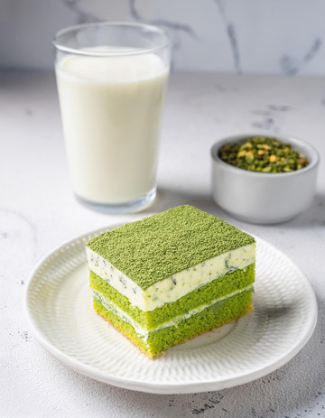 一块放在白色盘子上夹着奶油和豆子的抹茶蛋糕旁边有一杯抹茶饮品2