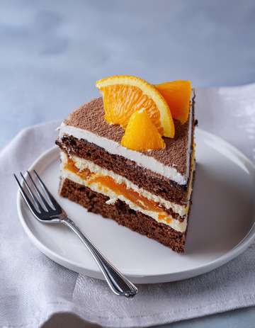 一块放在白色盘子上夹着奶油和橙子片顶部有巧克力片装饰的蛋糕旁边有把叉子4