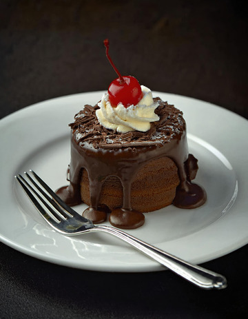 放在白色盘子上淋着巧克力酱顶部有颗樱桃和奶油的巧克力蛋糕2