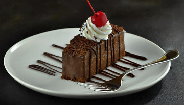 放在白色盘子上淋着巧克力酱顶部有颗樱桃和奶油的巧克力蛋糕1