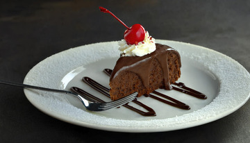 放在白色盘子上淋着巧克力酱顶部有颗樱桃和奶油的巧克力蛋糕3