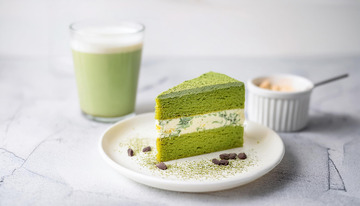 一块放在白色盘子上夹着奶油和豆子的抹茶蛋糕旁边有一杯抹茶饮品