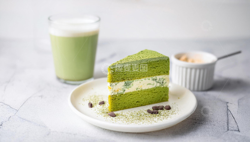 高清大图下载【趣麦麦图】一块放在白色盘子上夹着奶油和豆子的抹茶蛋糕旁边有一杯抹茶饮品