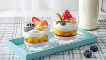 装在透明杯子里的水果奶油杯放在浅蓝色托盘上旁边有一瓶牛奶2