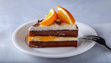 一块放在白色盘子上夹着奶油和橙子片顶部有巧克力片装饰的蛋糕旁边有把叉子3