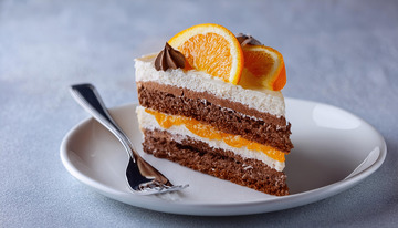 一块放在白色盘子上夹着奶油和橙子片顶部有巧克力片装饰的蛋糕旁边有把叉子